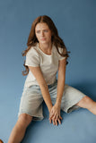 Woman sitting on a blue background wearing a striped shirt and denim skirt.