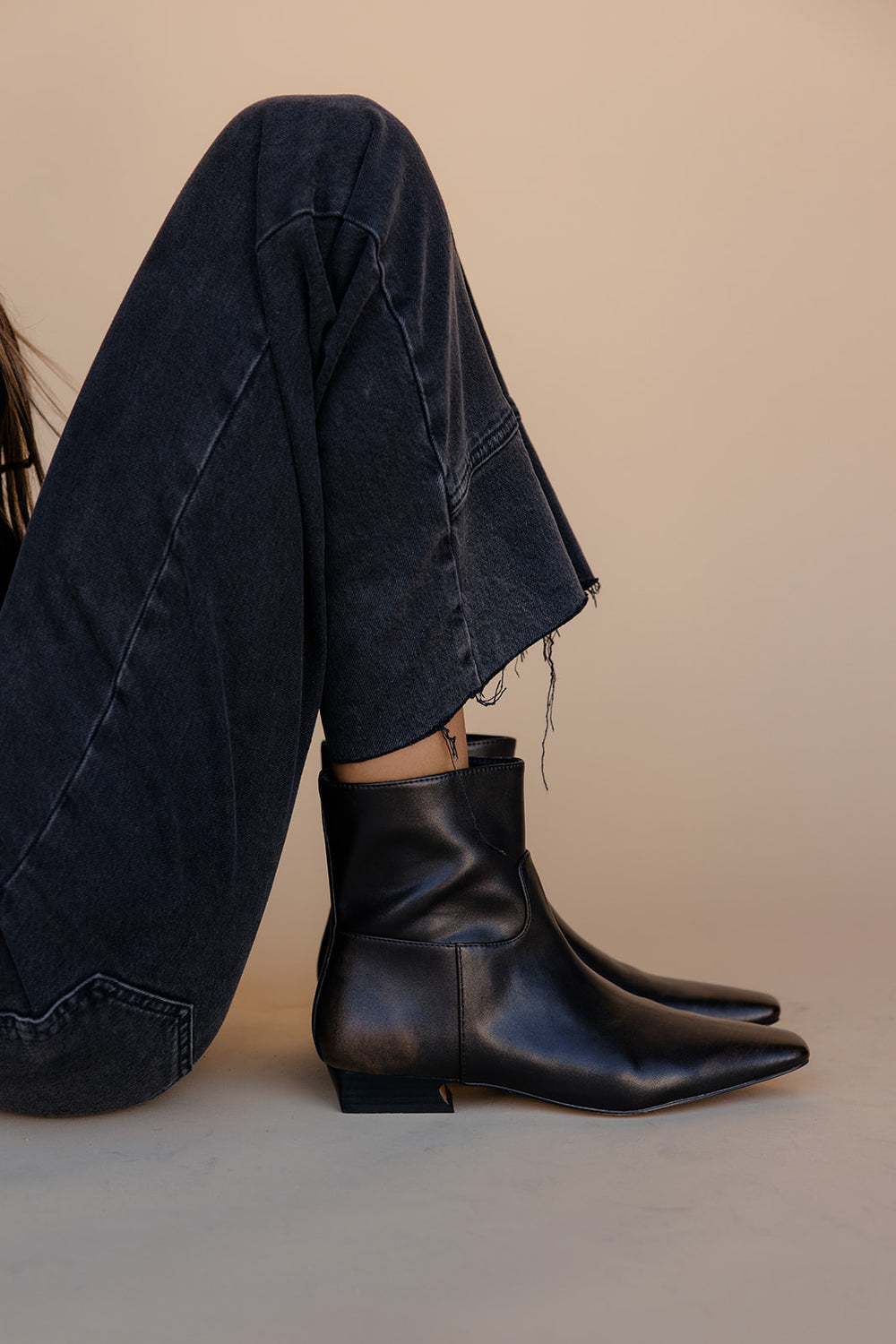 Person wearing brown leather ankle boots and dark jeans on a beige background