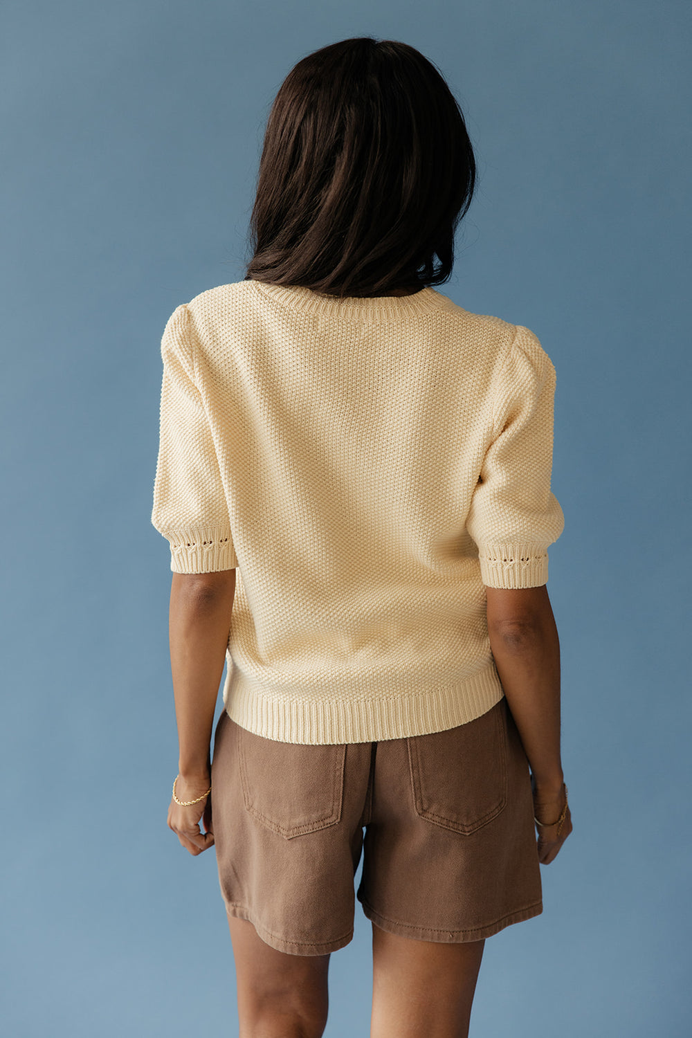 Woman wearing a short sleeve sweater against a blue background