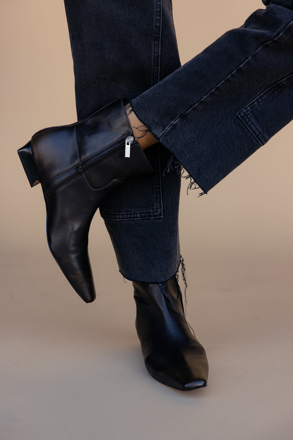 Brown leather ankle boots worn with dark jeans on a beige background