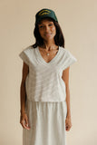 Woman wearing a white striped dress and green cap against a beige background
