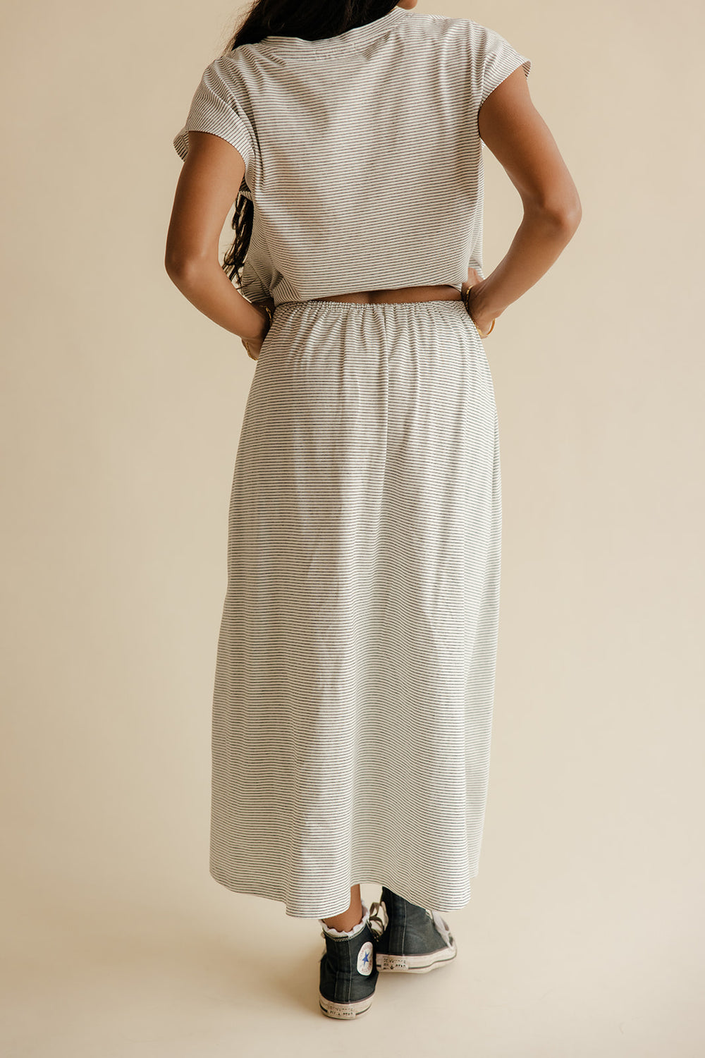Person wearing a matching top and skirt set with black sneakers on a beige background