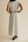 Person wearing a matching top and skirt set with black sneakers on a beige background