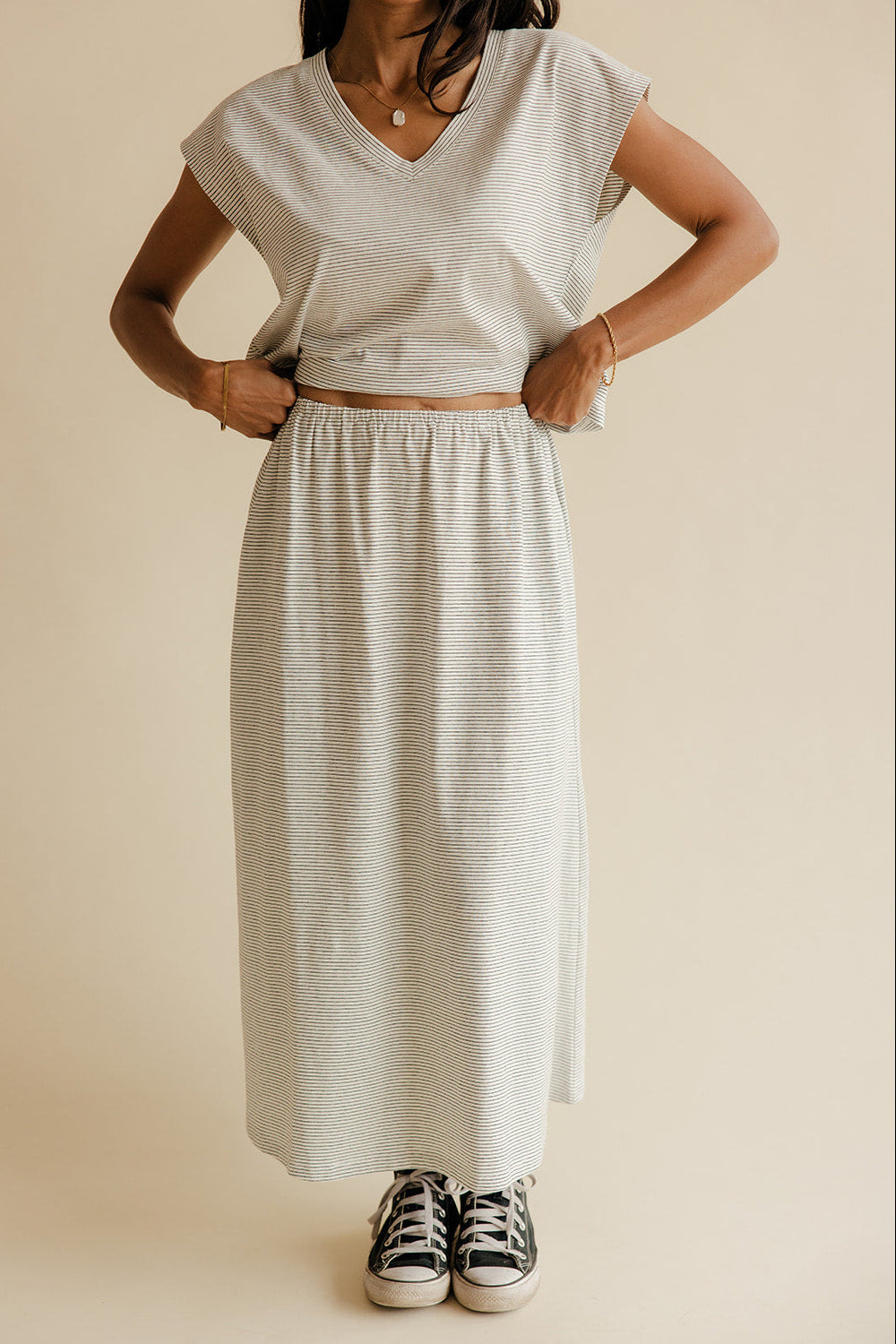 Person wearing a light gray top and skirt with black and white sneakers on a beige background