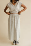 Person wearing a light gray top and skirt with black and white sneakers on a beige background
