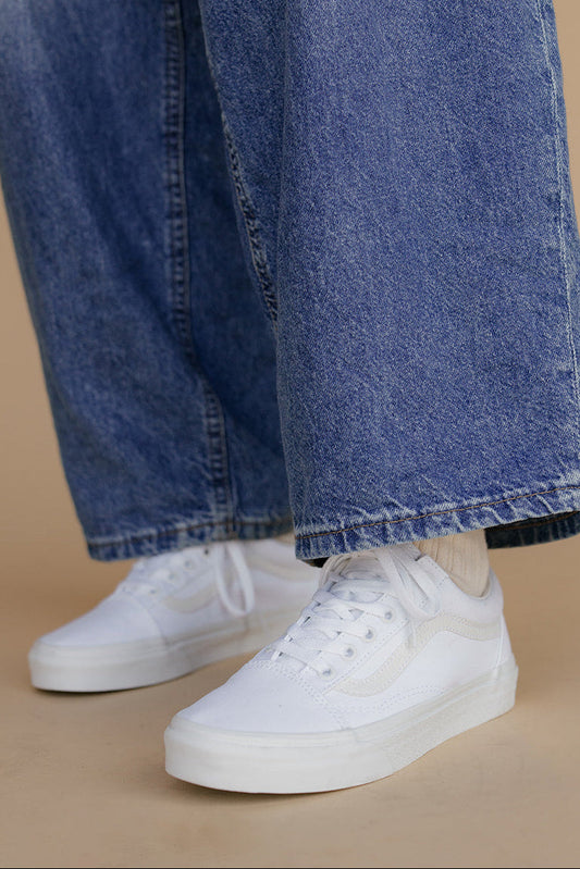 Person wearing blue jeans and white sneakers on a beige background