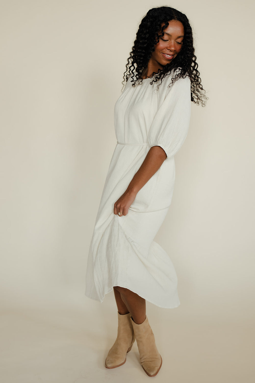 Woman wearing a white dress with beige boots on a plain background