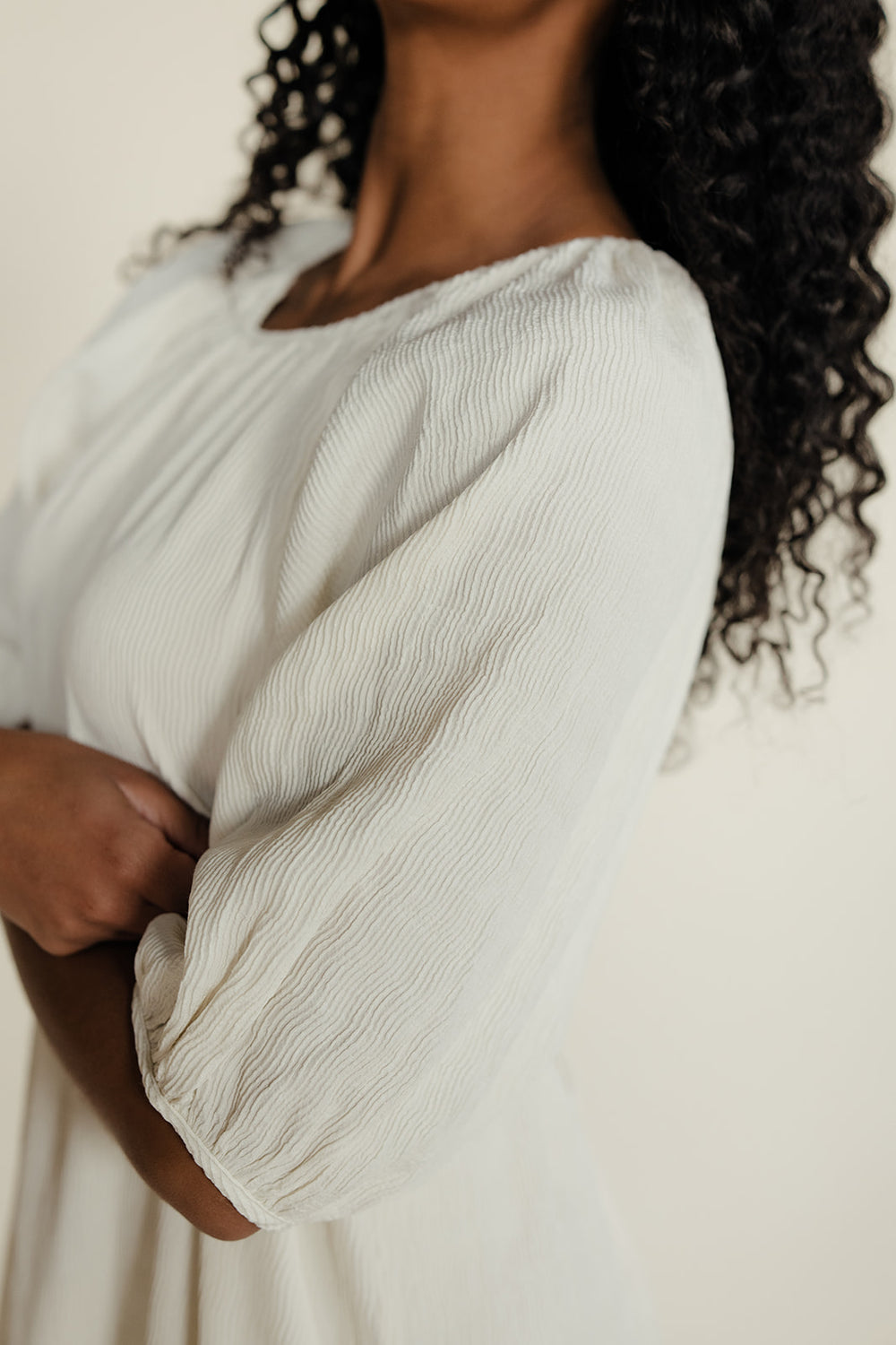 Close-up of a person wearing a light-colored dress with a neutral background
