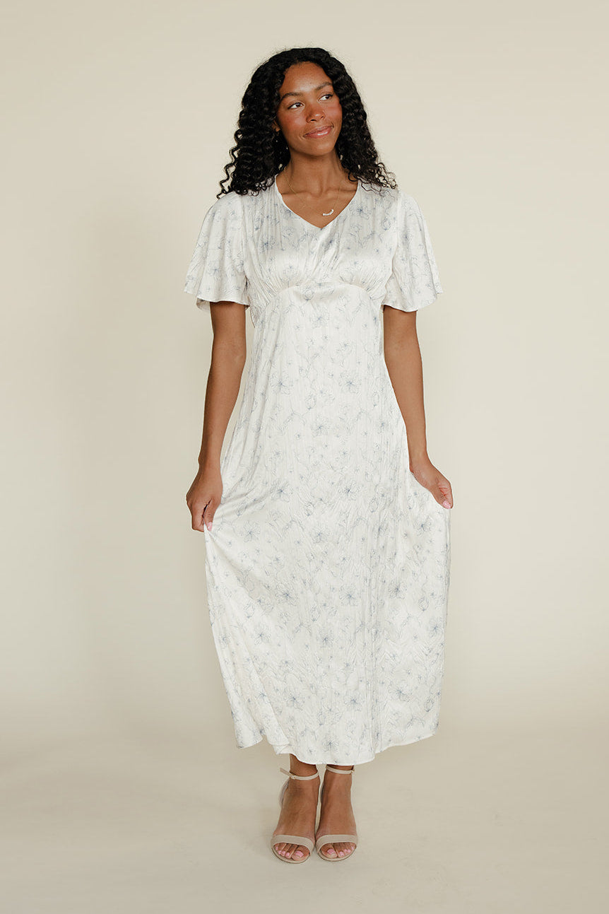 Woman wearing a white floral dress against a plain background