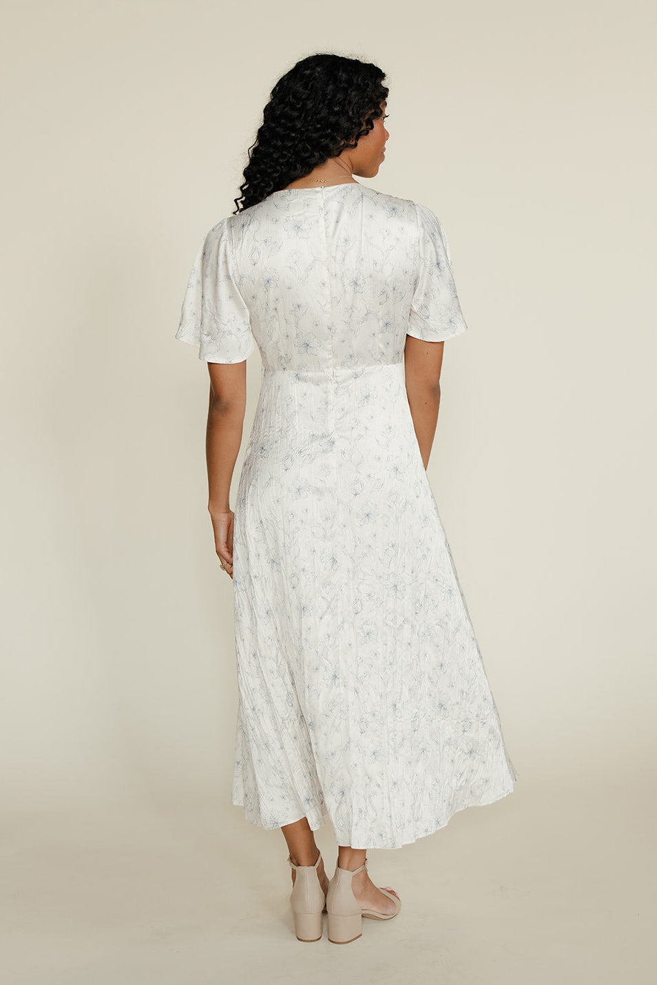 Woman wearing a white floral dress against a beige background