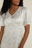 Woman wearing a light-colored dress with a subtle pattern on a plain background