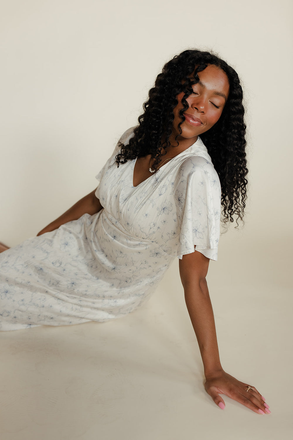 Woman in a light-colored dress sitting on a beige surface with a neutral background