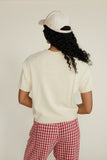 Person wearing a white t-shirt and red checkered pants with a white cap on a plain background
