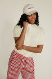 Woman wearing a white cap and button-up shirt with red checkered pants on a plain background