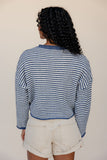 Person wearing a blue and white striped sweater and beige shorts against a plain background