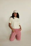 Woman wearing a white shirt and red checkered shorts with a beige cap on a plain background