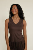 Woman wearing a brown sleeveless top and dark pants against a beige background