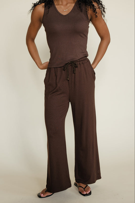 Woman wearing a brown sleeveless top and wide-leg pants on a plain background