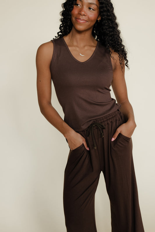 Woman wearing a brown sleeveless top and wide-leg pants against a beige background