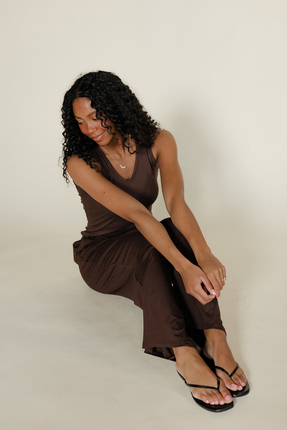 Woman wearing a brown jumpsuit sitting on a white background