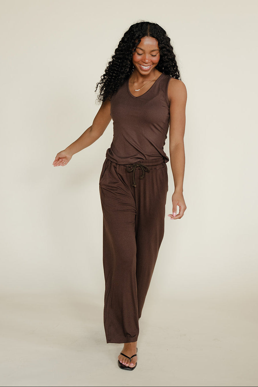 Woman wearing a brown sleeveless top and pants on a beige background