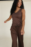 Woman wearing a brown sleeveless top and pants against a plain background