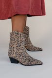 Leopard print boots worn with a red checkered skirt on a neutral background