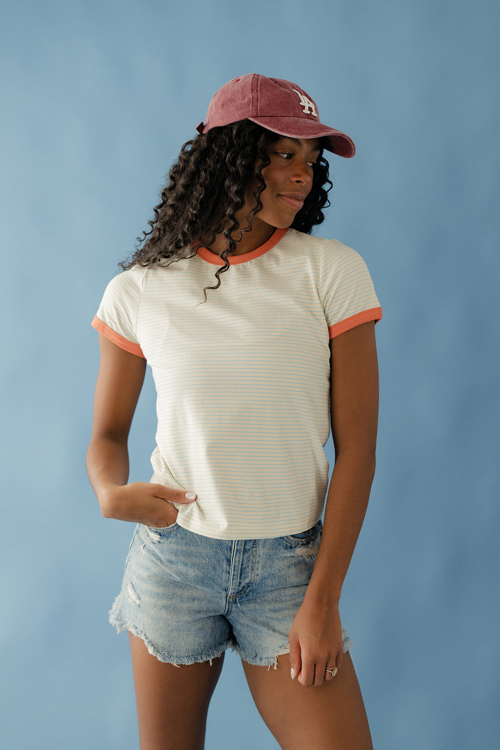 Woman wearing a white t-shirt with orange trim and denim shorts against a blue background