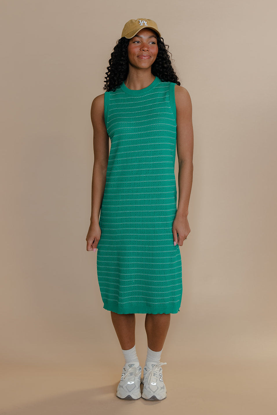 Woman wearing a green striped dress and white sneakers on a beige background