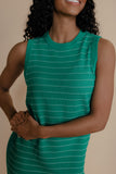 Woman wearing a green sleeveless dress with white stripes against a beige background