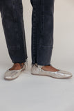 Person wearing dark jeans and metallic loafers on a plain background