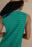 Person wearing a green sleeveless top with white stitching on a beige background