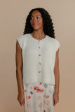 Woman wearing a light-colored knitted vest over a patterned skirt on a beige background