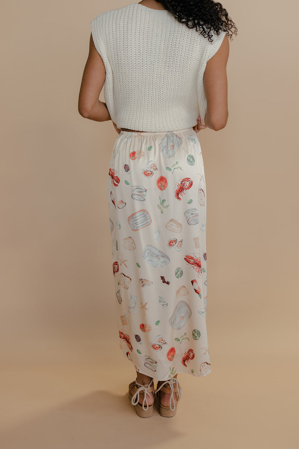 Person wearing a white sleeveless top and a long, patterned skirt on a beige background
