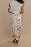 Person wearing a white sleeveless top and a long, patterned skirt on a beige background