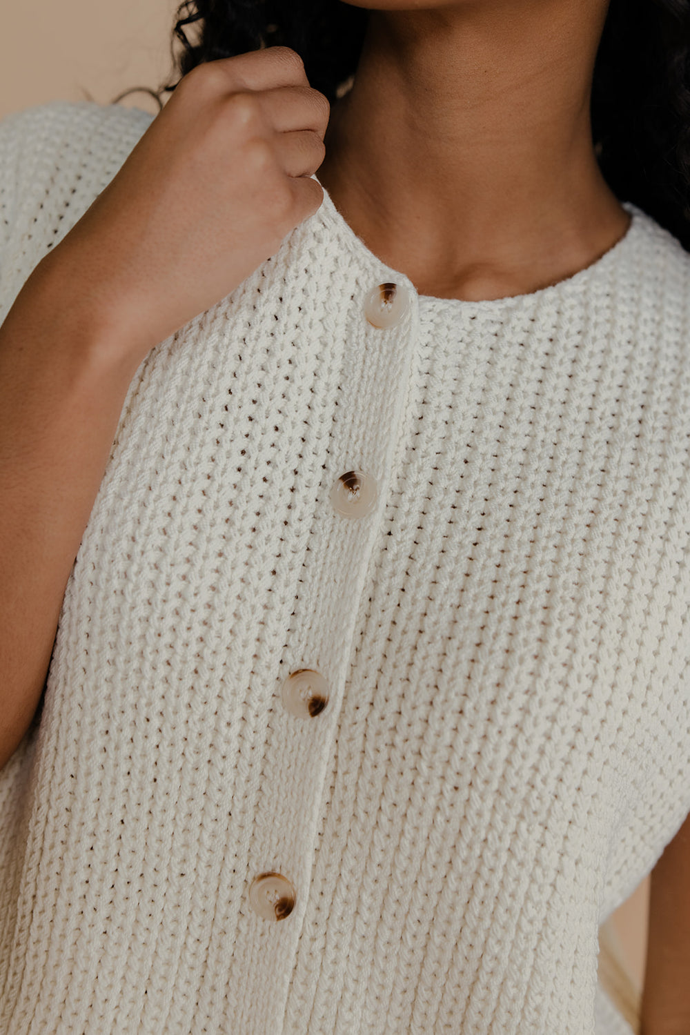 Close-up of a person wearing a beige knitted cardigan with wooden buttons.