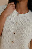 Close-up of a person wearing a beige knitted cardigan with wooden buttons.