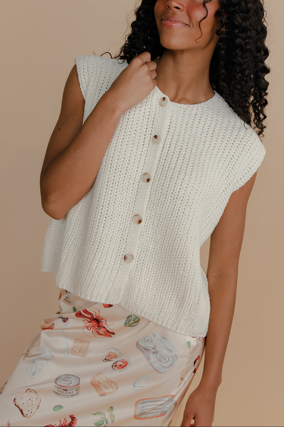 Woman wearing a white knitted sleeveless top against a beige background