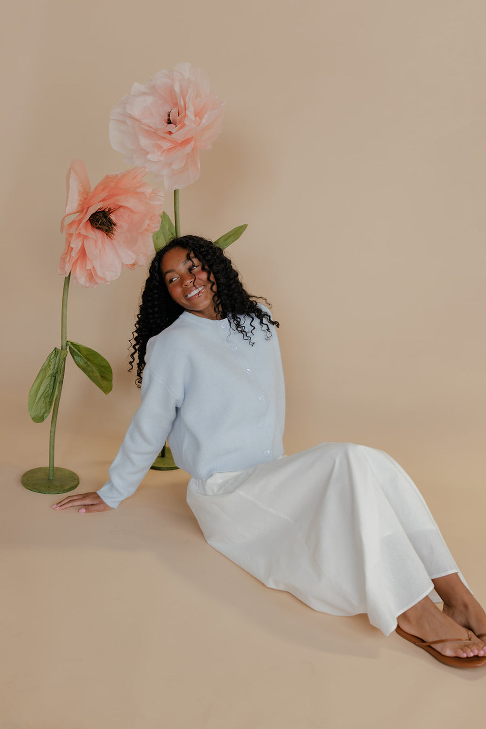 Woman sitting on a beige floor with large flowers behind her