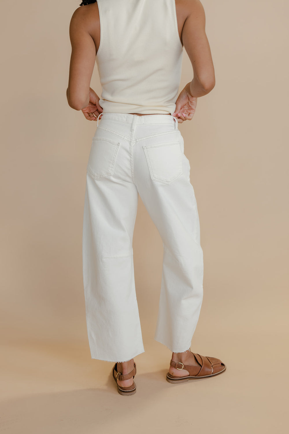 Person wearing a white tank top and wide-leg pants on a beige background