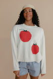 Woman wearing a white sweater with red tomato designs on a beige background