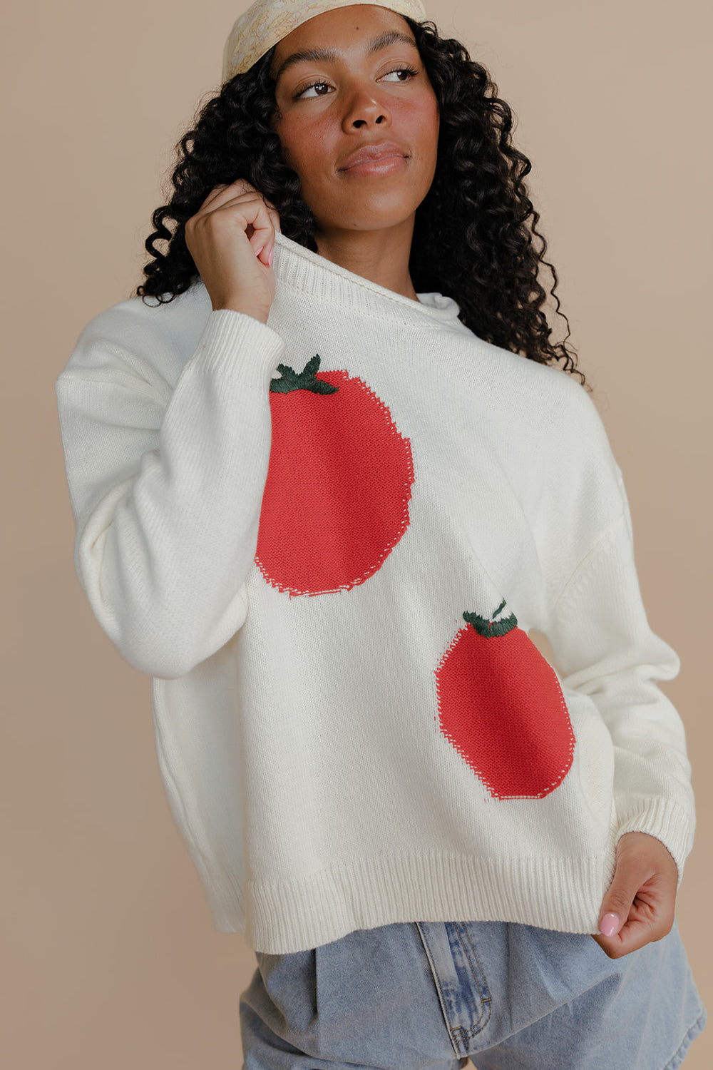 Woman wearing a cream sweater with red tomato designs on a beige background
