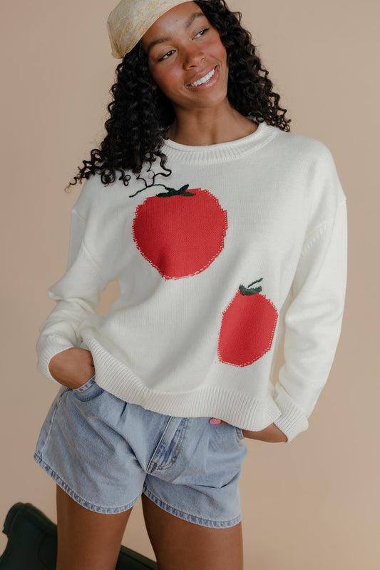 Person wearing a white sweater with red tomato designs on a beige background
