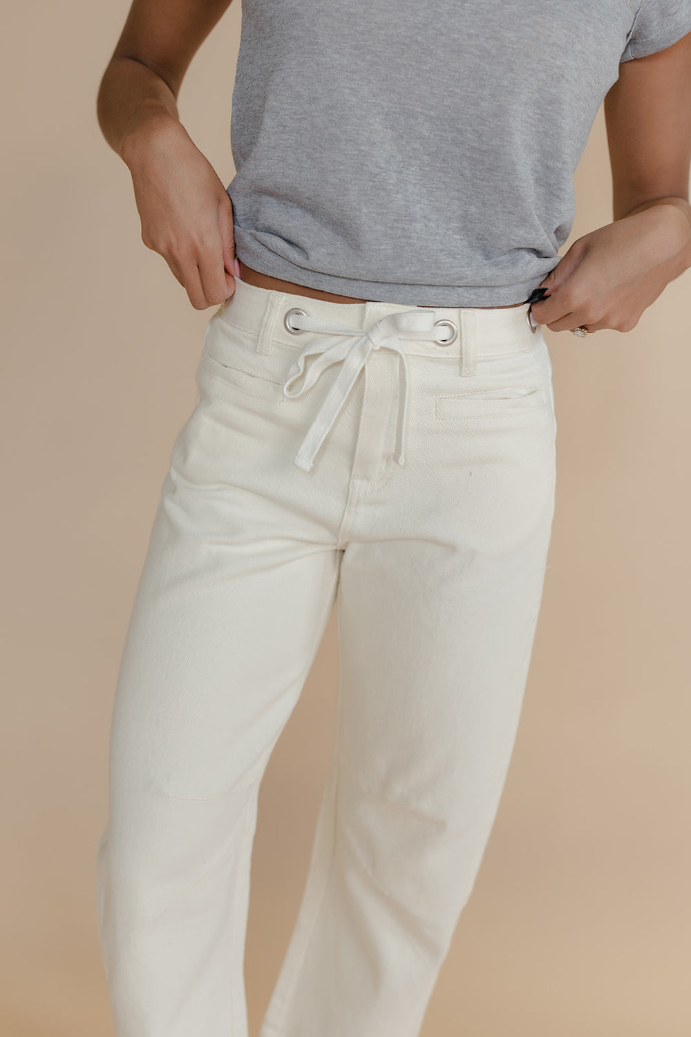 Person wearing white pants with a drawstring and a gray shirt on a beige background