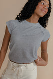 Woman wearing a gray t-shirt and white pants against a beige background