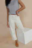 Person wearing a gray top and white pants on a beige background