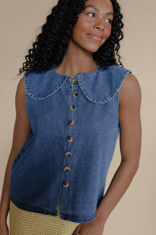 Woman wearing a blue denim sleeveless shirt with a collar on a beige background