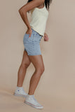 Person wearing light blue denim shorts and white sneakers on a beige background