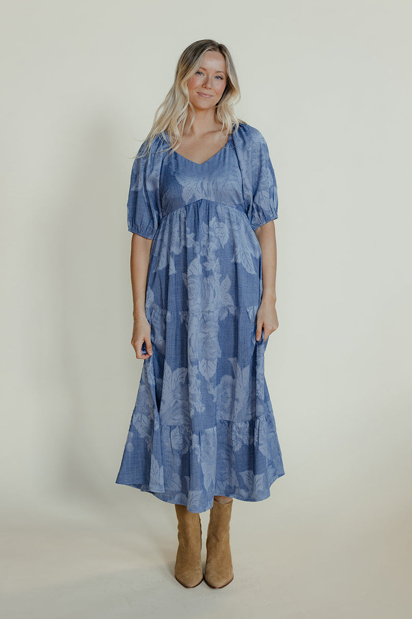 Woman wearing a blue patterned dress standing against a plain background