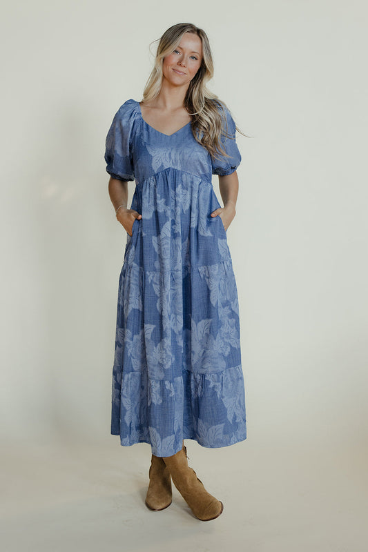 Woman wearing a blue floral dress with puffed sleeves against a white background